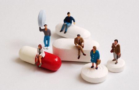 AM69E7  Group of tiny figures standing on sitting on and holding a variety of pills and capsules
